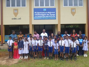 school building in Balangoda with students outside, classroom exterior at Thiruvalluvar Maha Vidyalayam, rural Sri Lankan school grounds, students standing on open field near school, two-storey school building front view, side view of school with painted wall murals, classroom block surrounded by greenery, students gathering during school hours